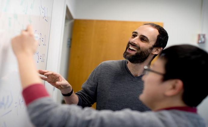 A Temple professor helping a student solve a ma的matics equation on a whiteboard in a classroom.